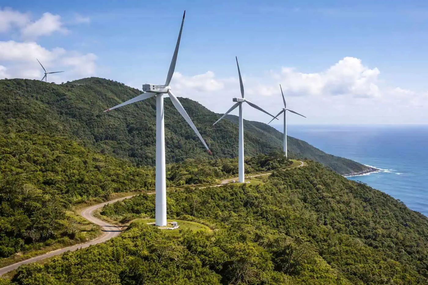 Een rij moderne witte windturbines op een groene heuvelrug langs de kust van een Kaapverdisch eiland, illustratie bij de ambitie voor 100% duurzame energie in 2030